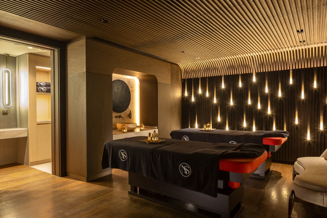 Couples treatment room with two side-by-side massage beds and candle-like wall lights