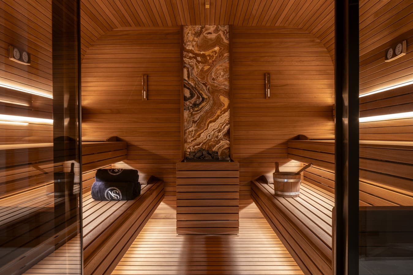 View through the glass door into the wood-lined Finnish sauna with Navitas towels on the bench