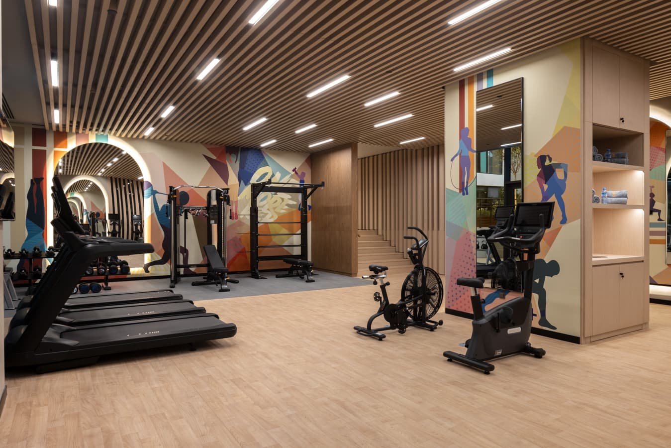 Corner of the gym with a treadmill, an air bike and a mirror under an illuminated arch