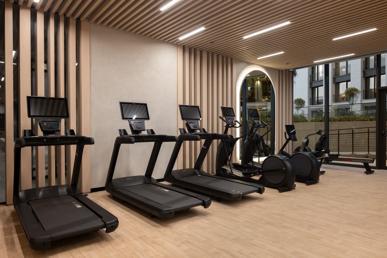 Row of treadmills and ellipticals with screens facing the windows