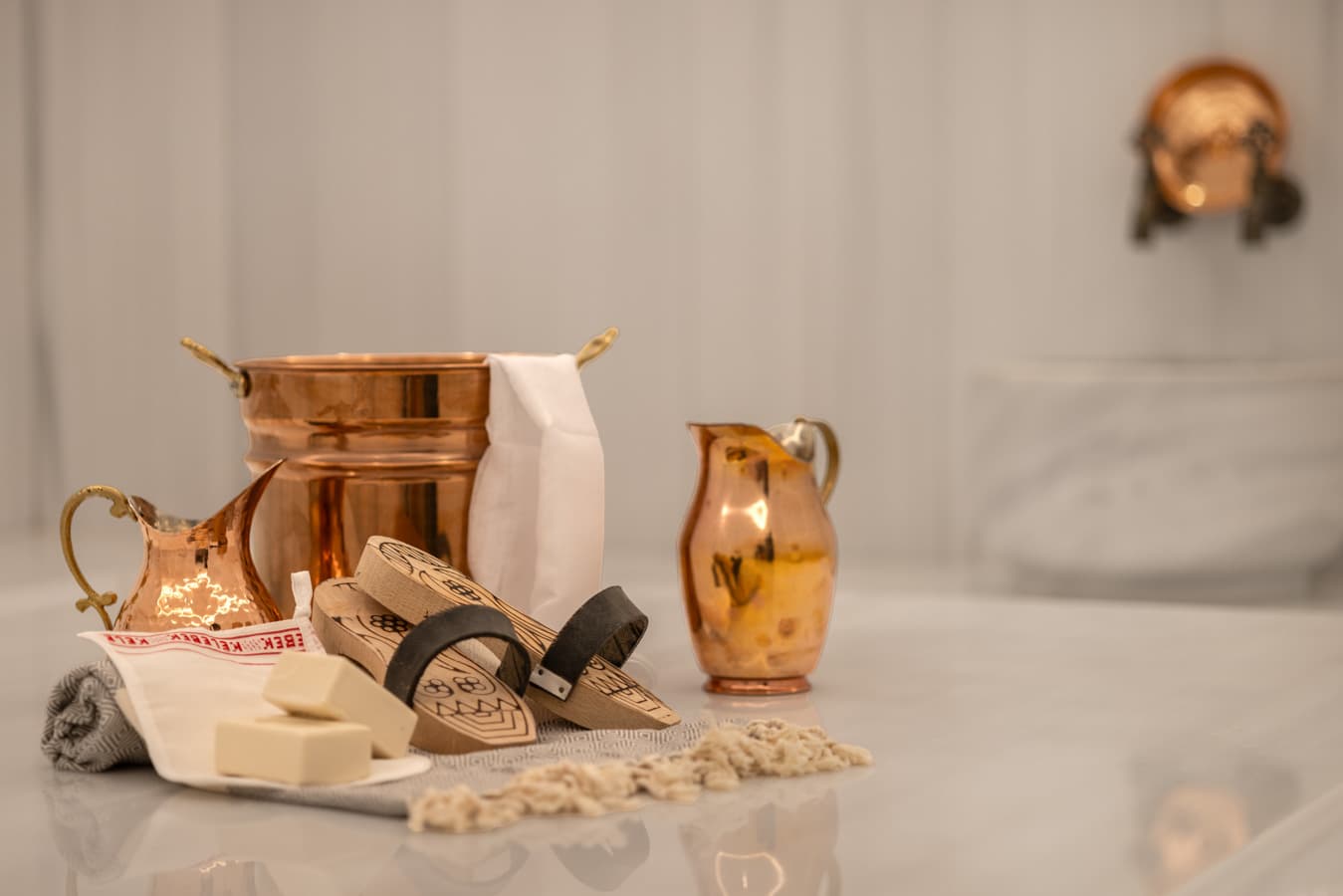Hammam set on the marble: copper bowl and jug, natural olive-oil soap, kese mitt, pestemal and wooden clogs