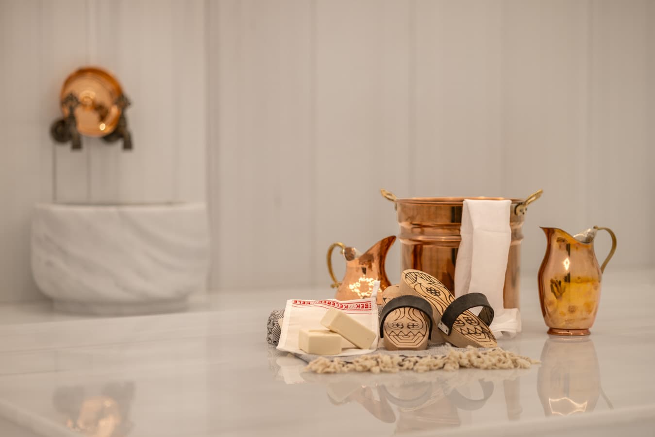Copper hammam bowls, soap and kese mitt laid out beside a marble basin before a scrub and foam ritual