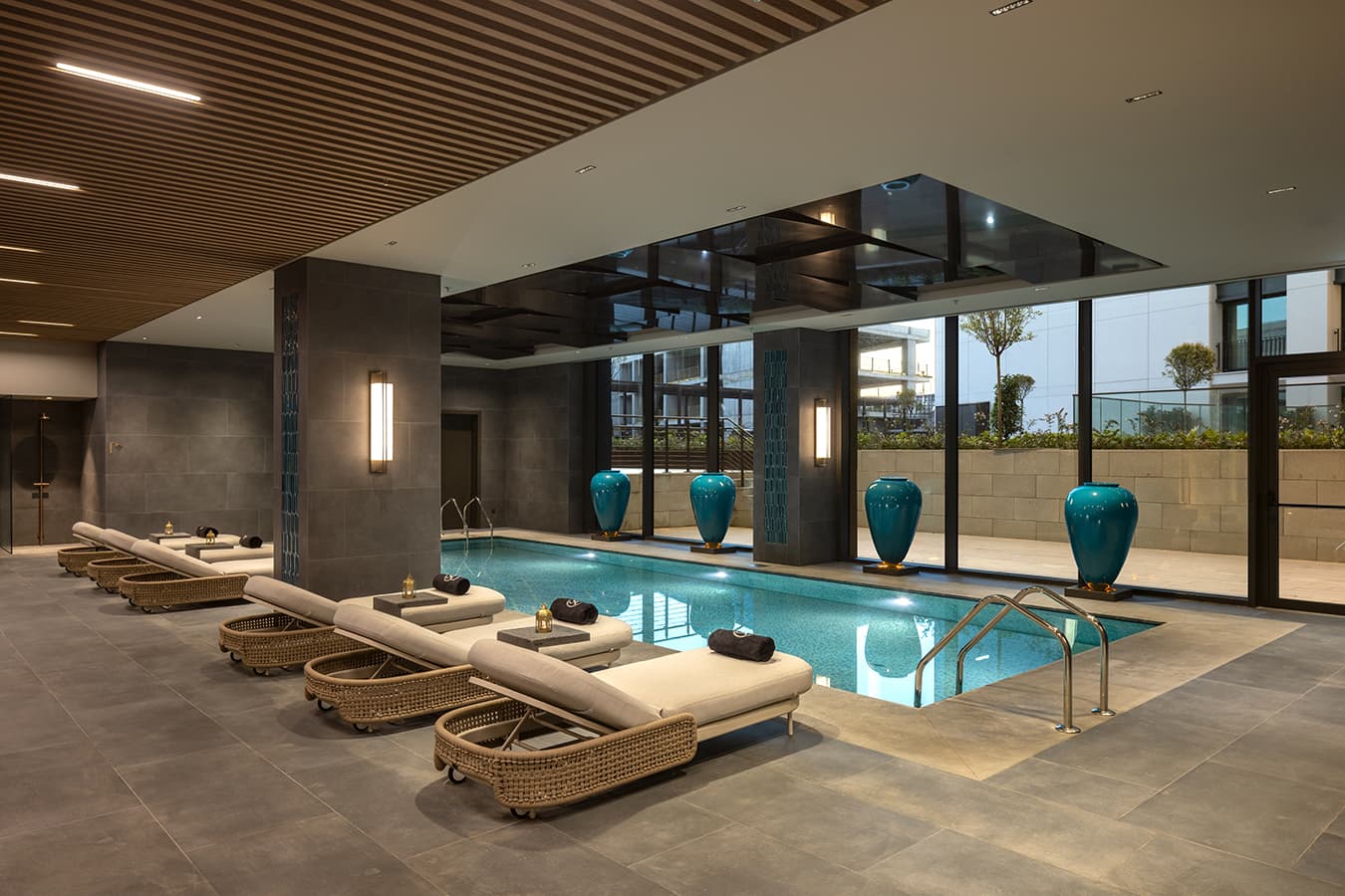 Heated indoor pool with rattan loungers, turquoise ceramic vases and tall windows