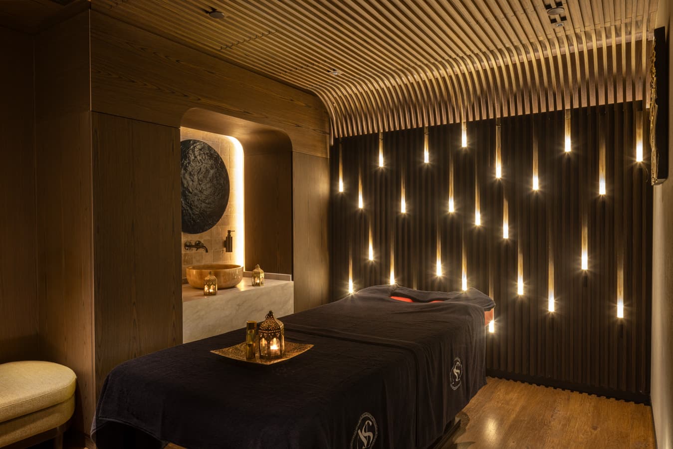 Single massage room with warm oak walls, a lit alcove with a copper bowl and a cushioned bench