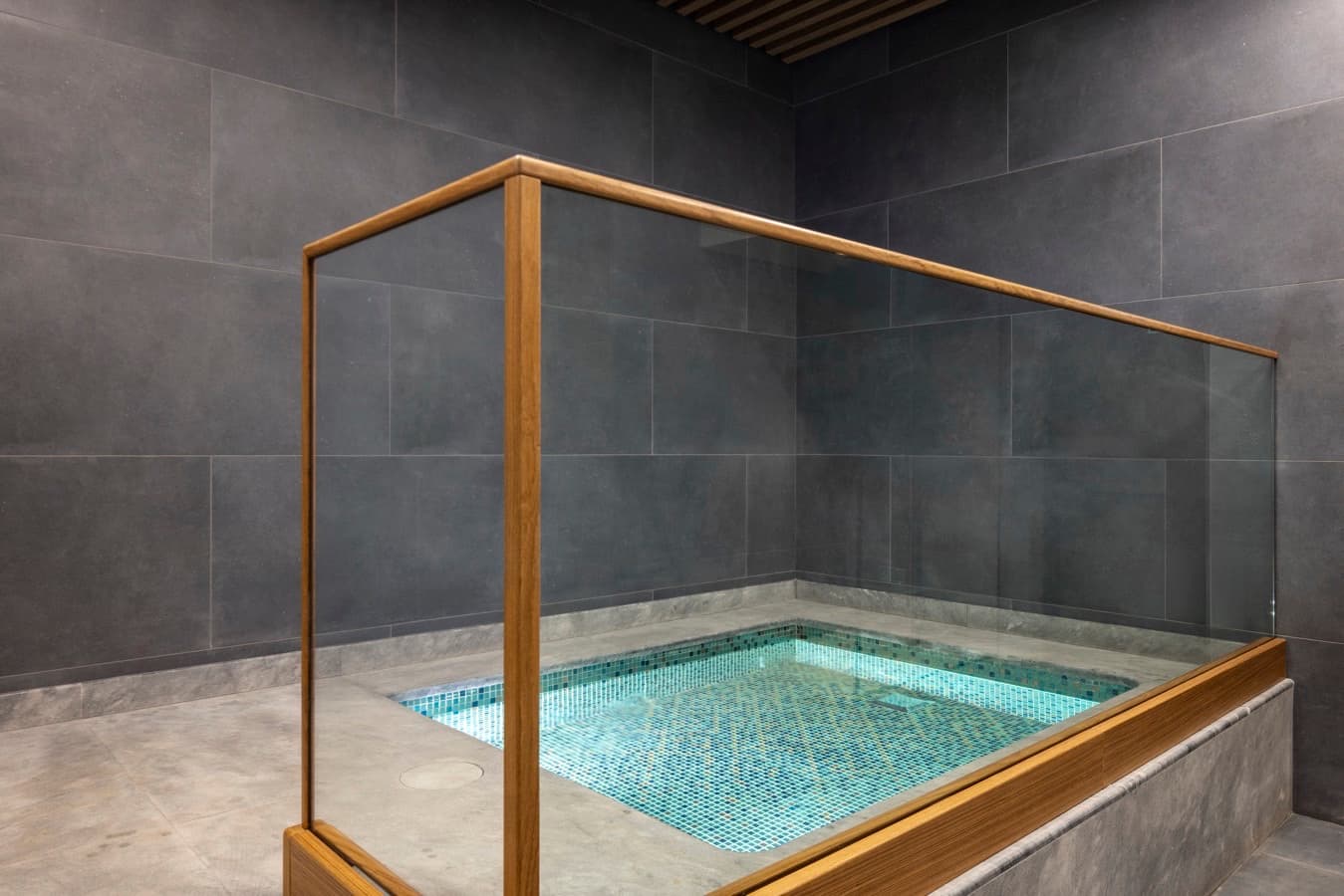 Plunge pool in turquoise mosaic behind a glass and oak balustrade