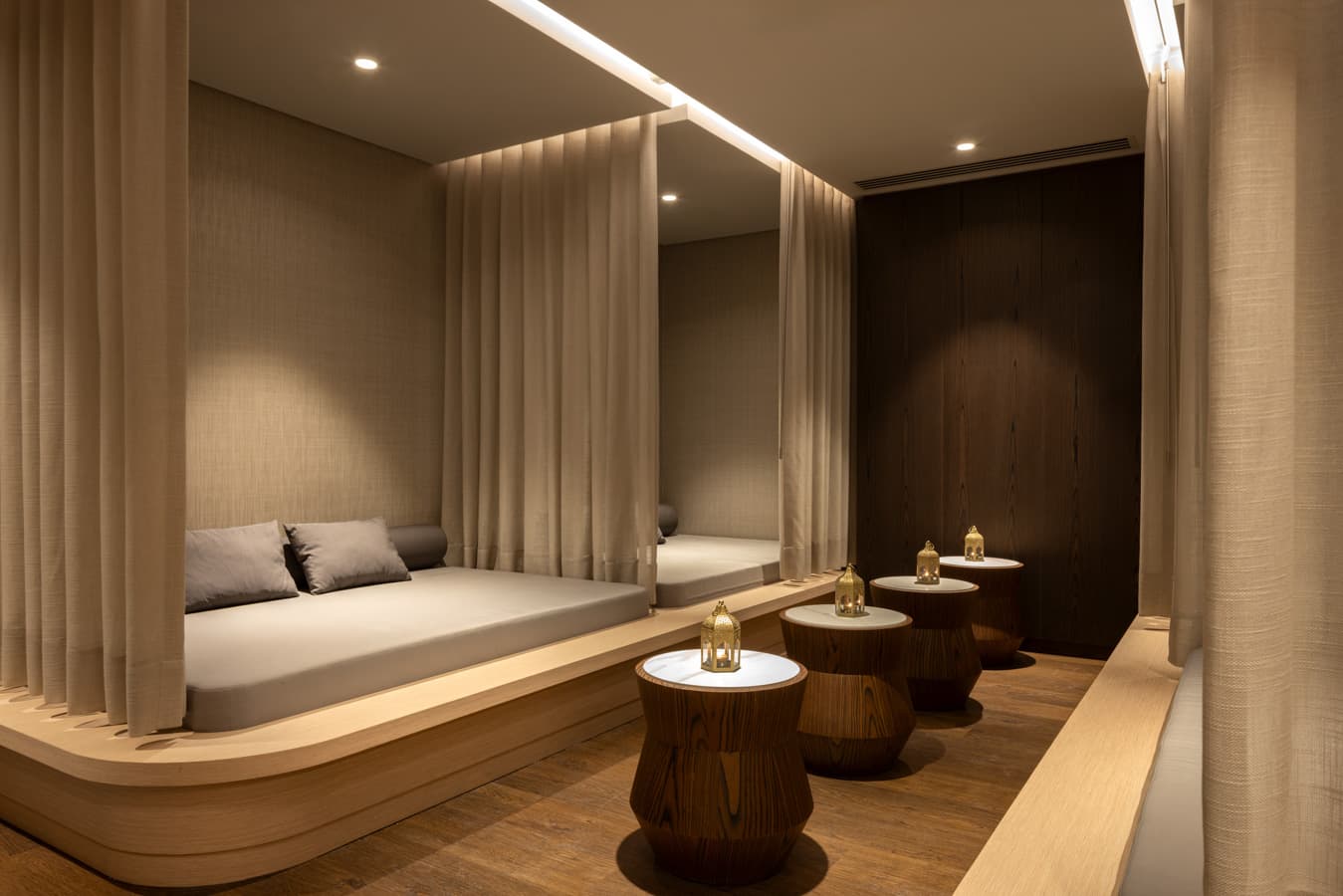 Curtained daybed alcove with cushions and a candle on a wooden side table in the relaxation lounge