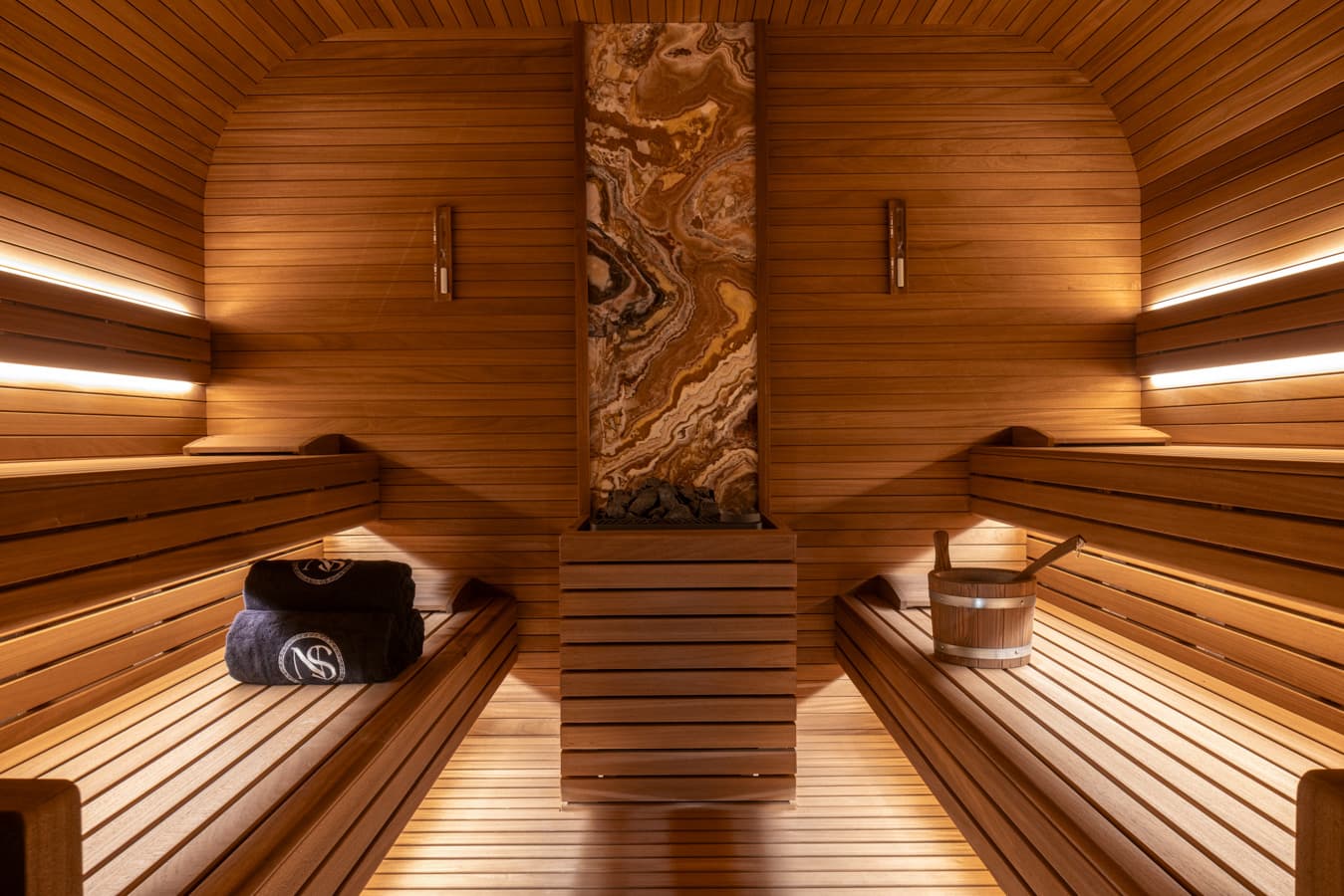 Finnish sauna clad in pale wood with tiered benches and a marble feature column at Navitas Spa Hilton Istanbul Airport
