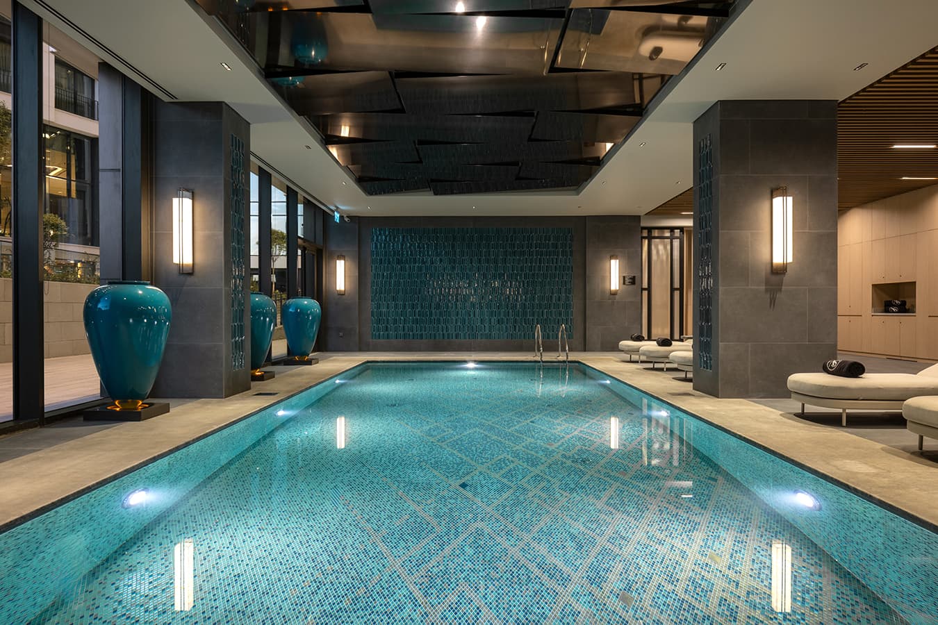 Long view of the indoor pool with a mirrored ceiling, patterned turquoise tiles and brass wall lights