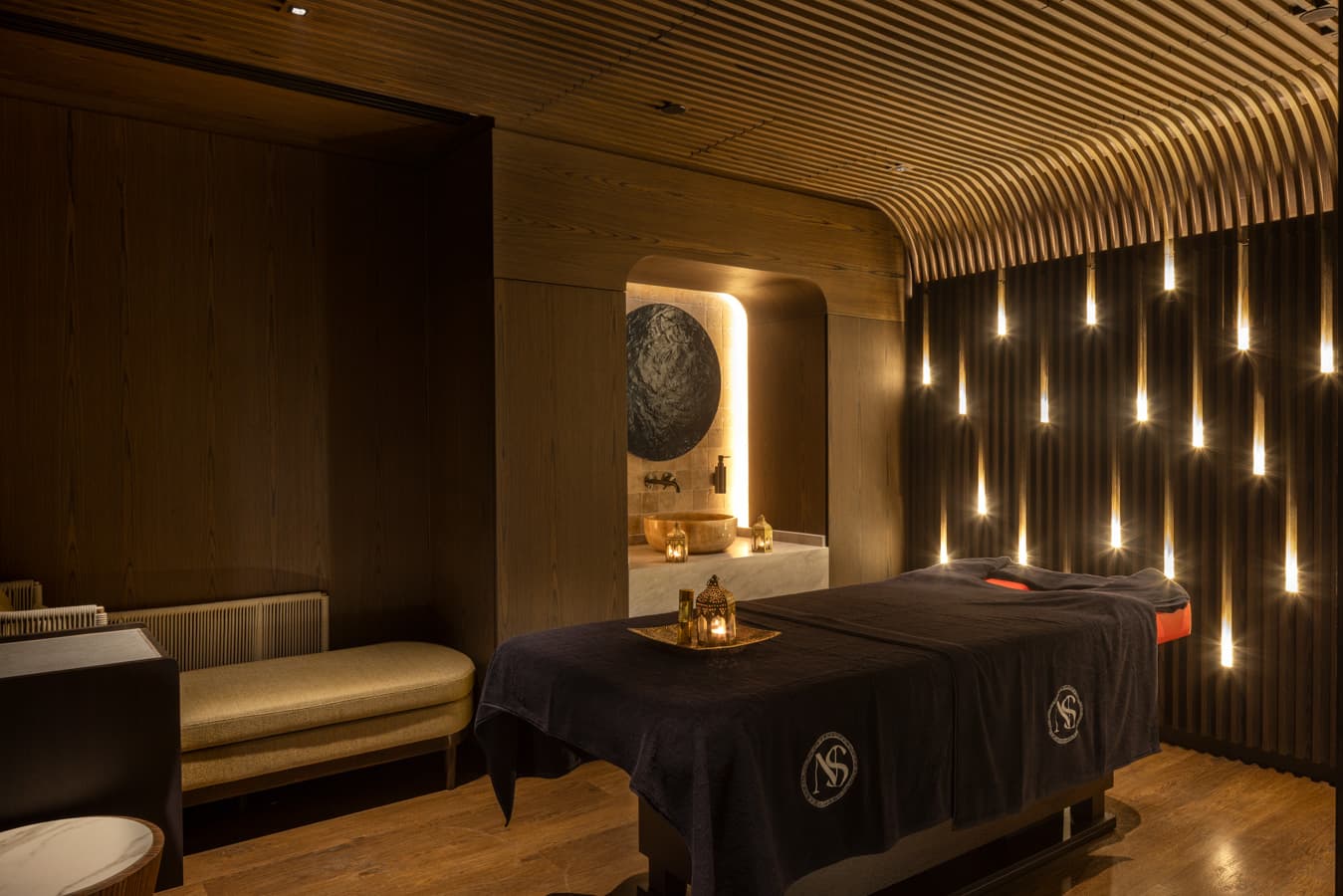 Single treatment room with a massage bed under a navy Navitas cover and a wall of candle-shaped lights