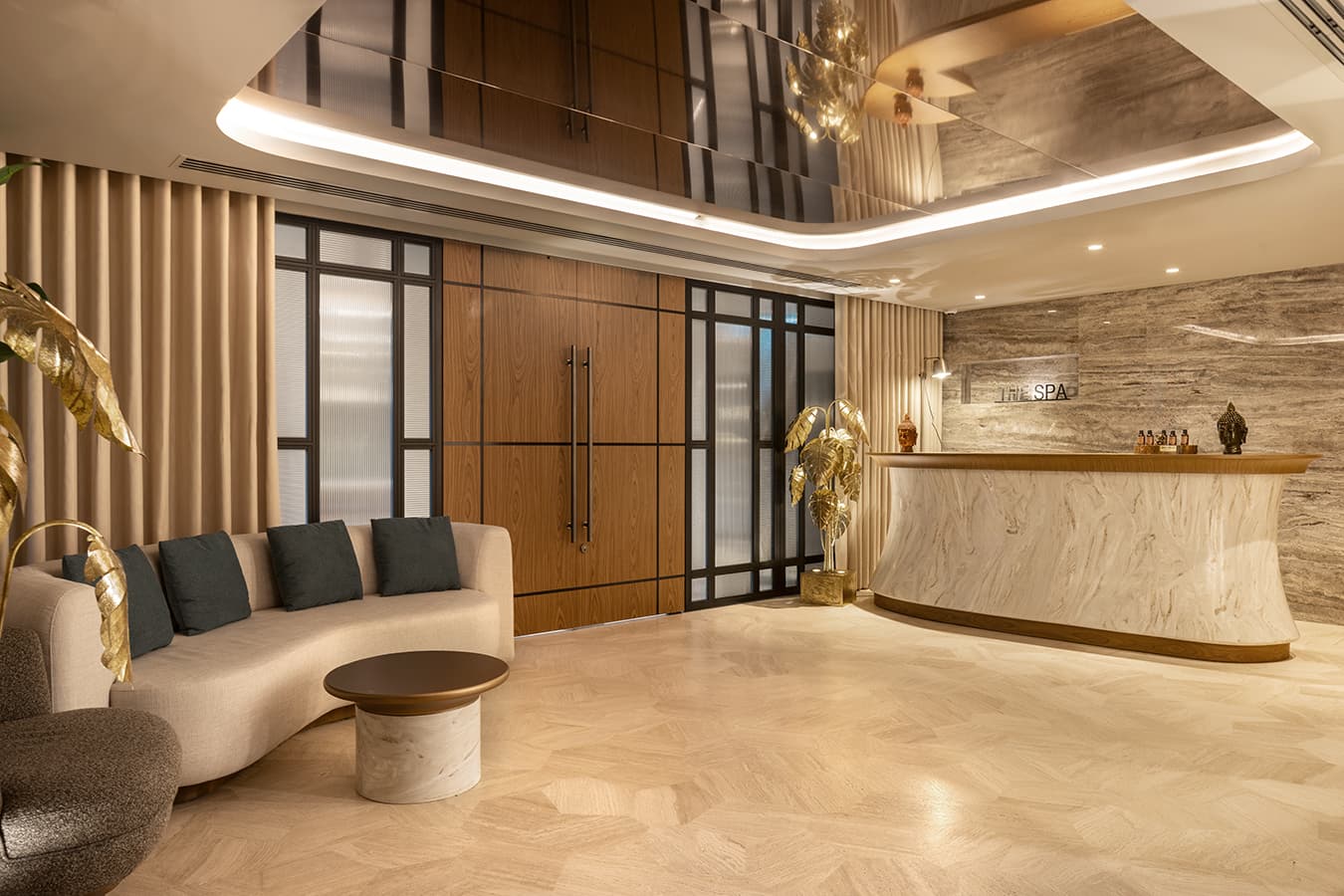 Spa reception with a curved marble desk, a cream sofa and a gold leaf sculpture under a lit ceiling