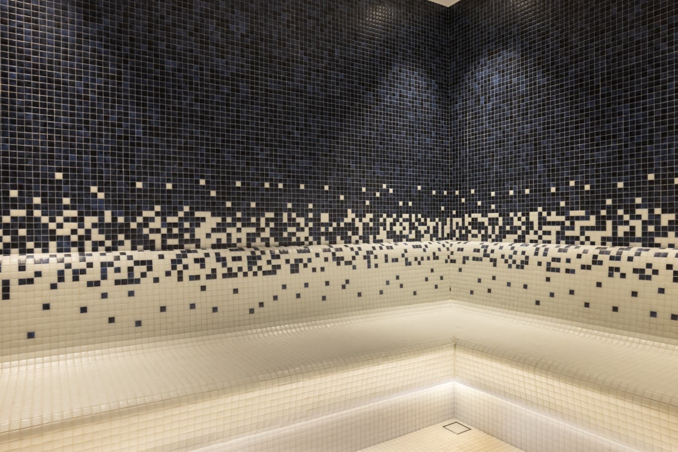 Mosaic-tiled steam room at Navitas Spa Hilton Istanbul Airport, navy tiles fading into white with lit marble benches